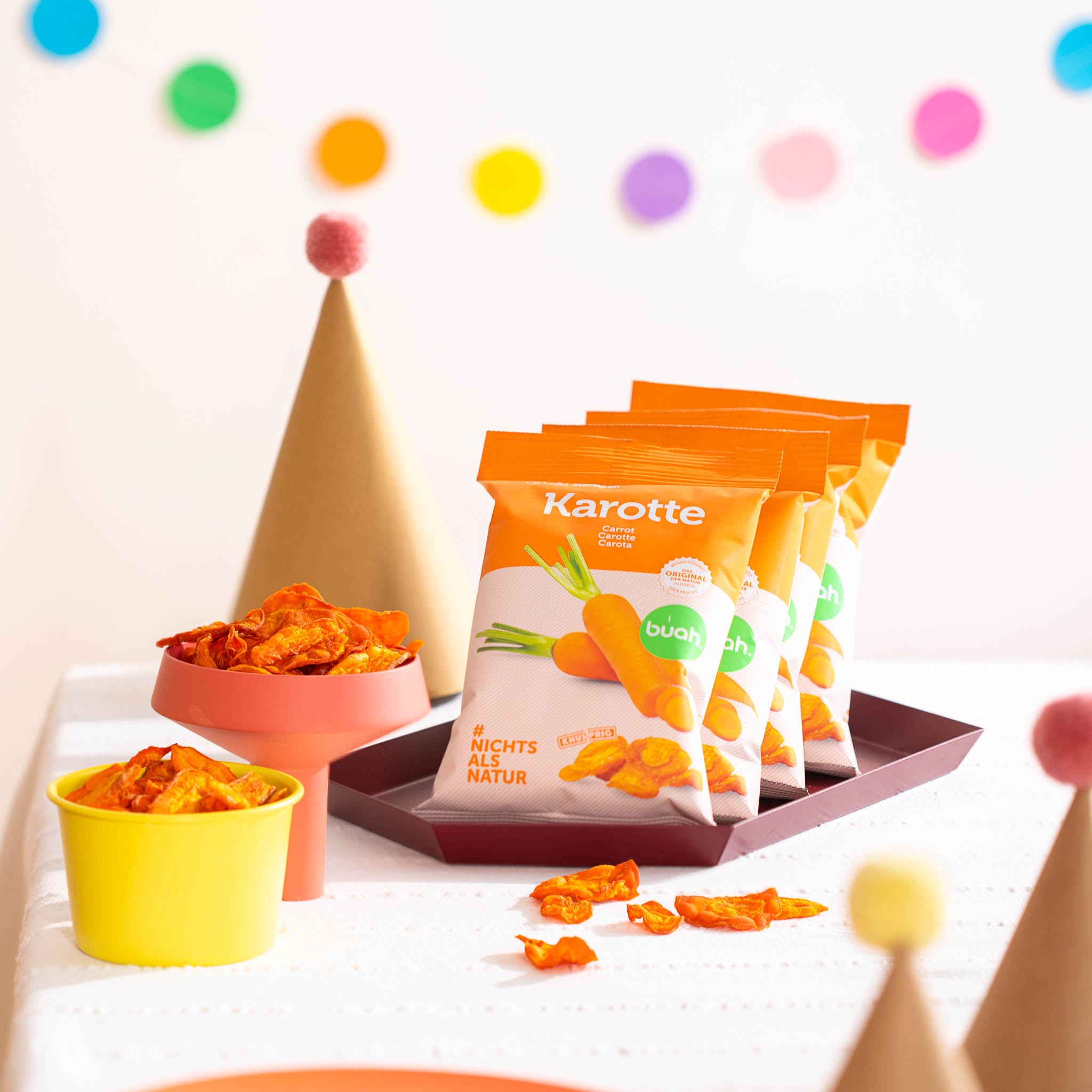 Packungen buah Karottenchips auf einem Geburtstagstisch mit Karottenchips in Schalen daneben