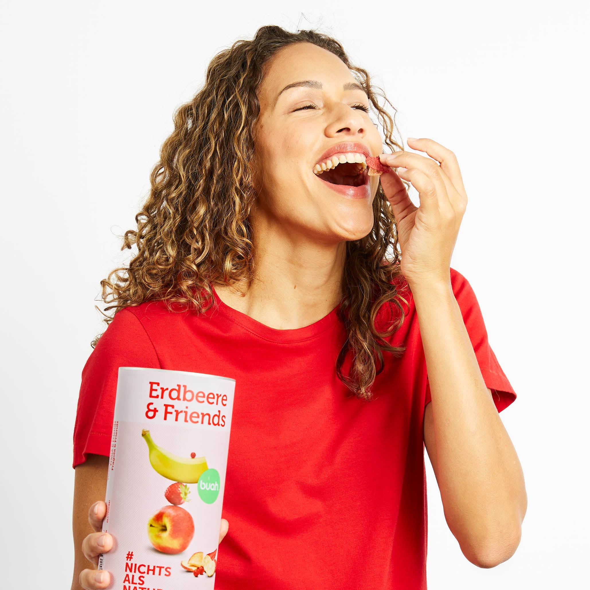 Lachende junge Frau im roten Shirt hat eine Dose buah Erdbeere & Friends in der Hand
