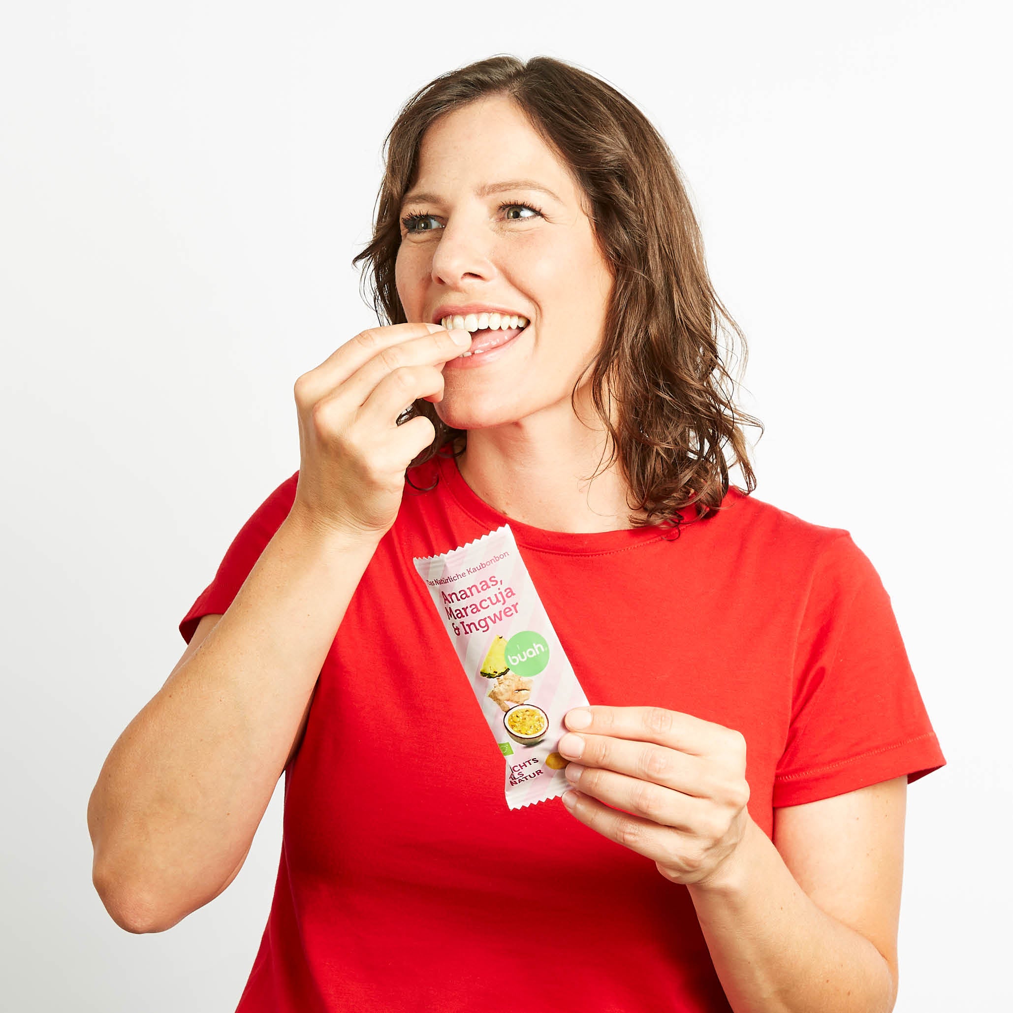 Mama in rotem Shirt hat eine Packung buah Ananas-Maracuja Kaubonbons in der Hand und isst diese