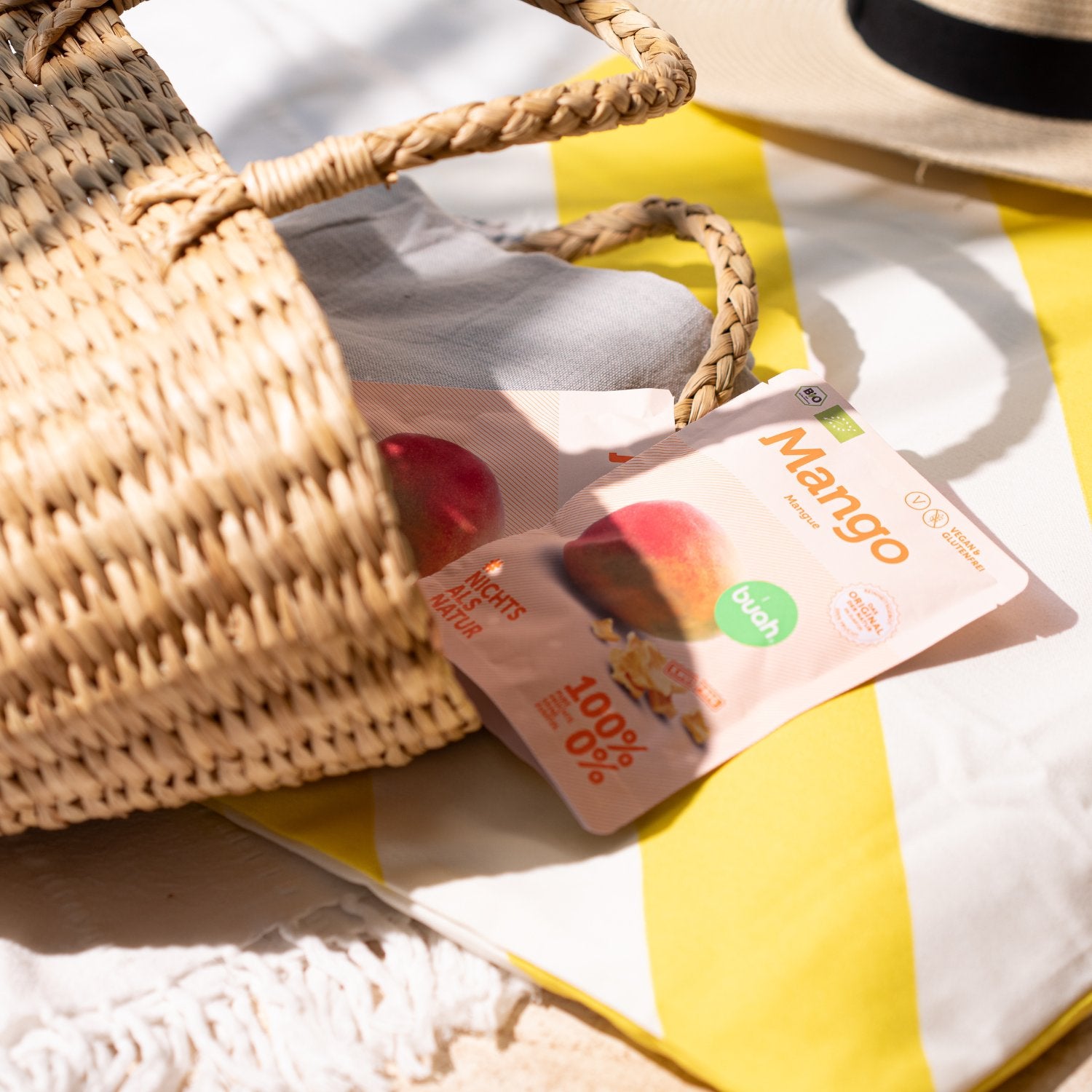 Mango Snackpack von buah ragt aus Picknickkorb der auf einer Picknick Decke liegt