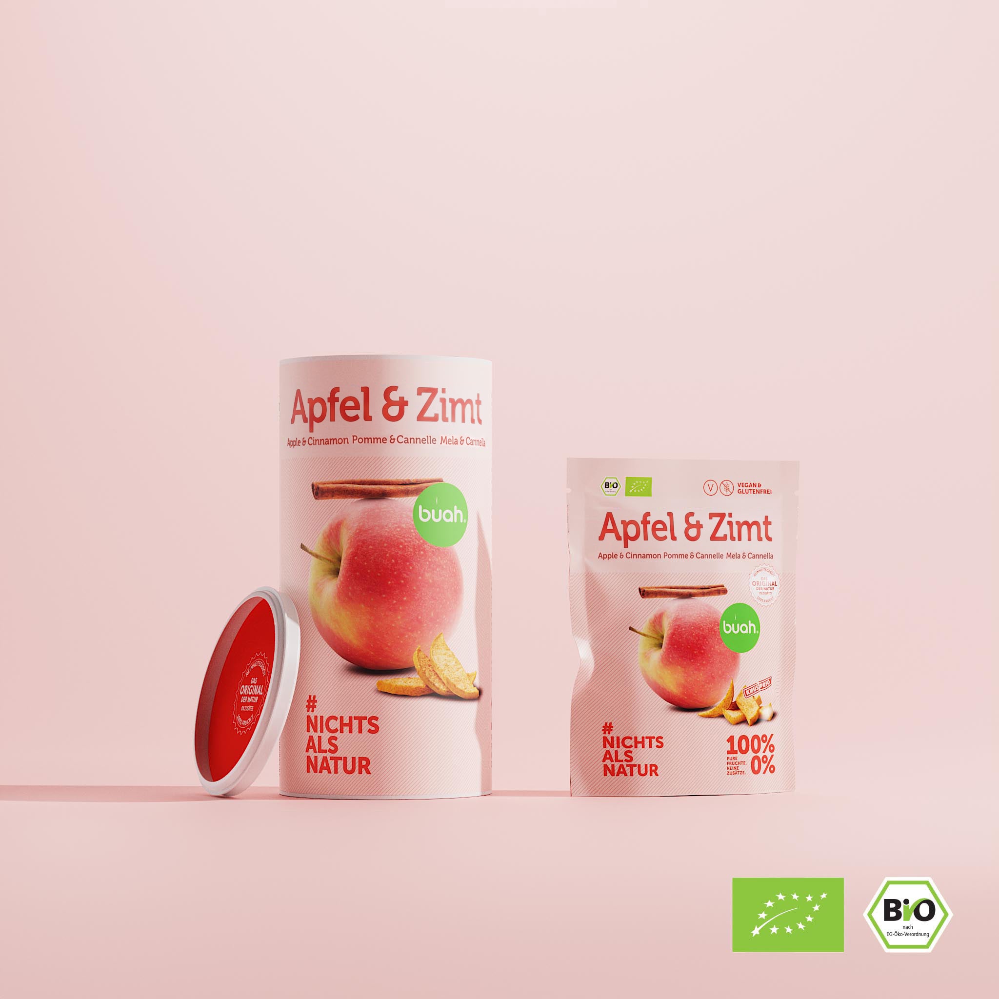Eine große Dose und ein kleiner Beutel buah gefriergetrocknete Früchte der Sorte Apfel & Zimt stehen nebeneinander vor einem rosa Hintergrund. Ein roter Deckel lehnt seitlich an der Dose.