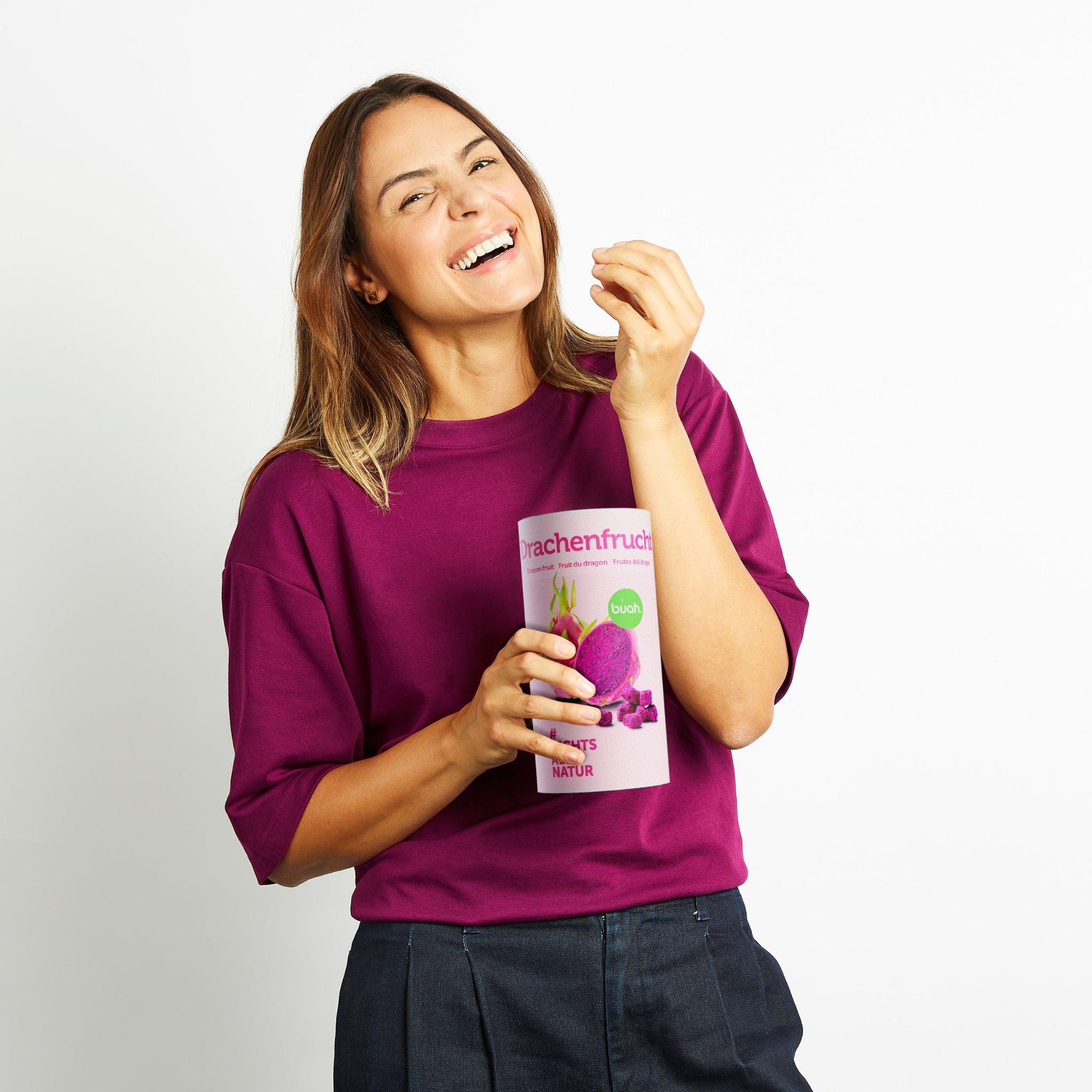 Junge Frau mit lila Shirt lacht in die Kamera und snackt aus einer Dose buah gefriergetrockneter Drachenfrucht