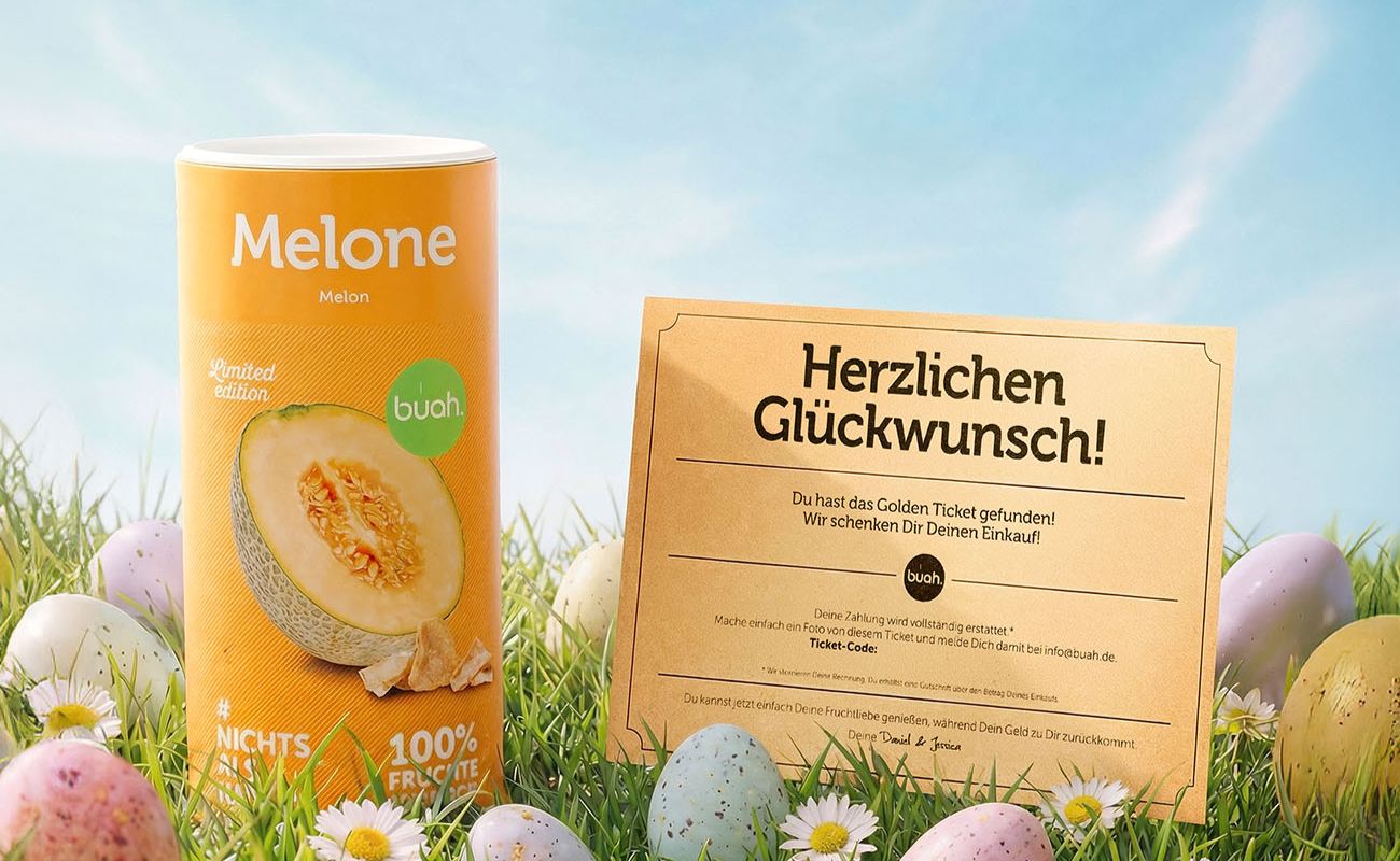 buah Aktion golden Ticket. Ein goldenes Papier-Ticket steht auf einer gruenen Wiese neben einer Dose buah gefriergetrocknete Cantaloupe Melone. Im Gras liegen Ostereier.