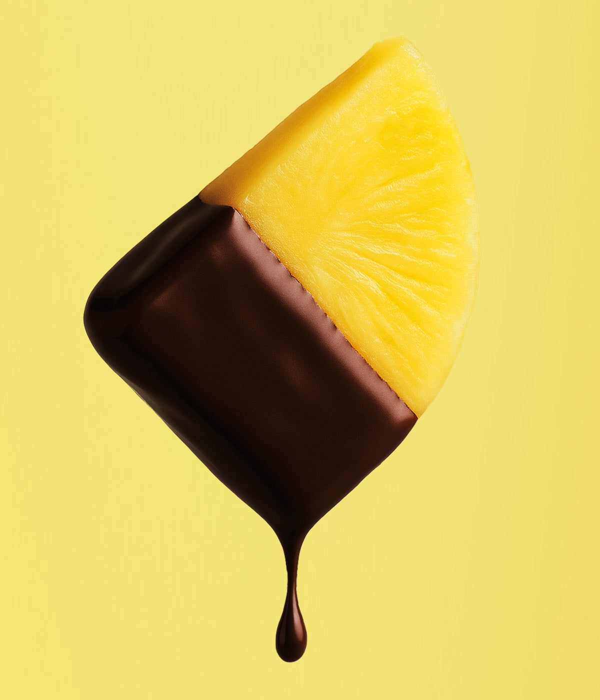 Eine gelbe Ananasspalte wird in flüssige, dunkle 100% Kakaomasse getaucht vor einem sonnengelben Hintergrund