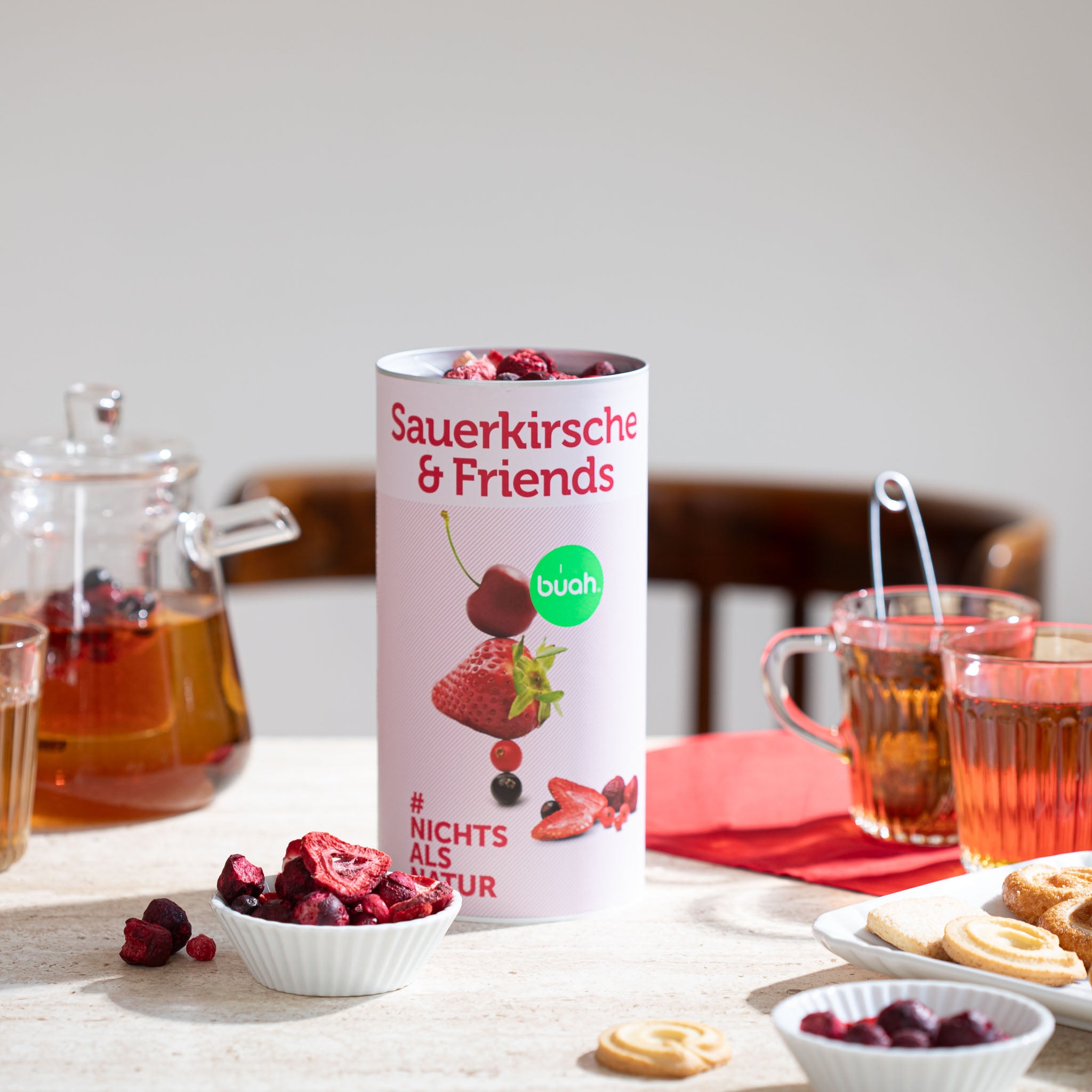 buah Dose Sauerkirsche & Friends steht auf Tisch neben Teekanne und Teeglaesern