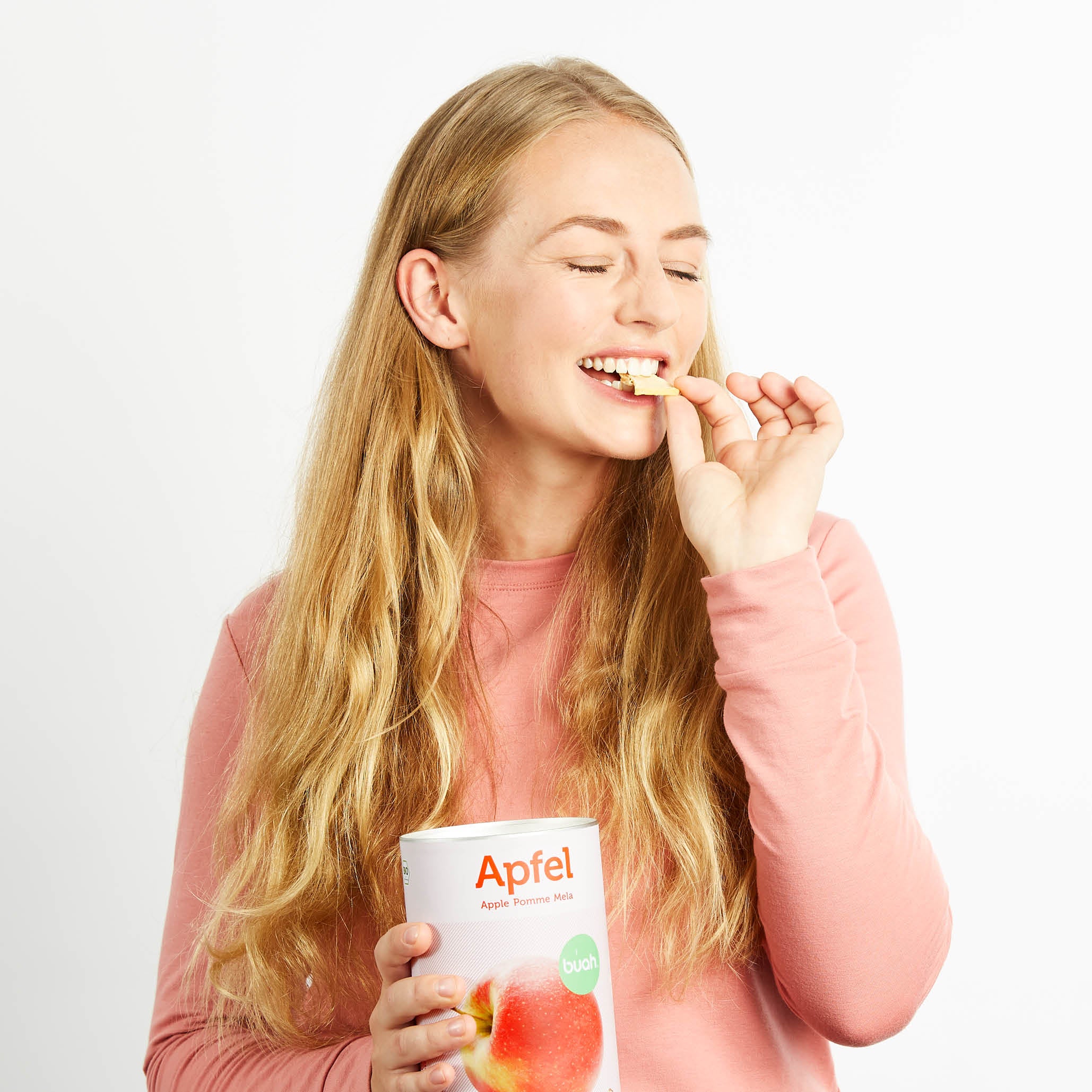 Junge Frau mit blonden Haaren hat eine Dose buah Apfel und isst diesen