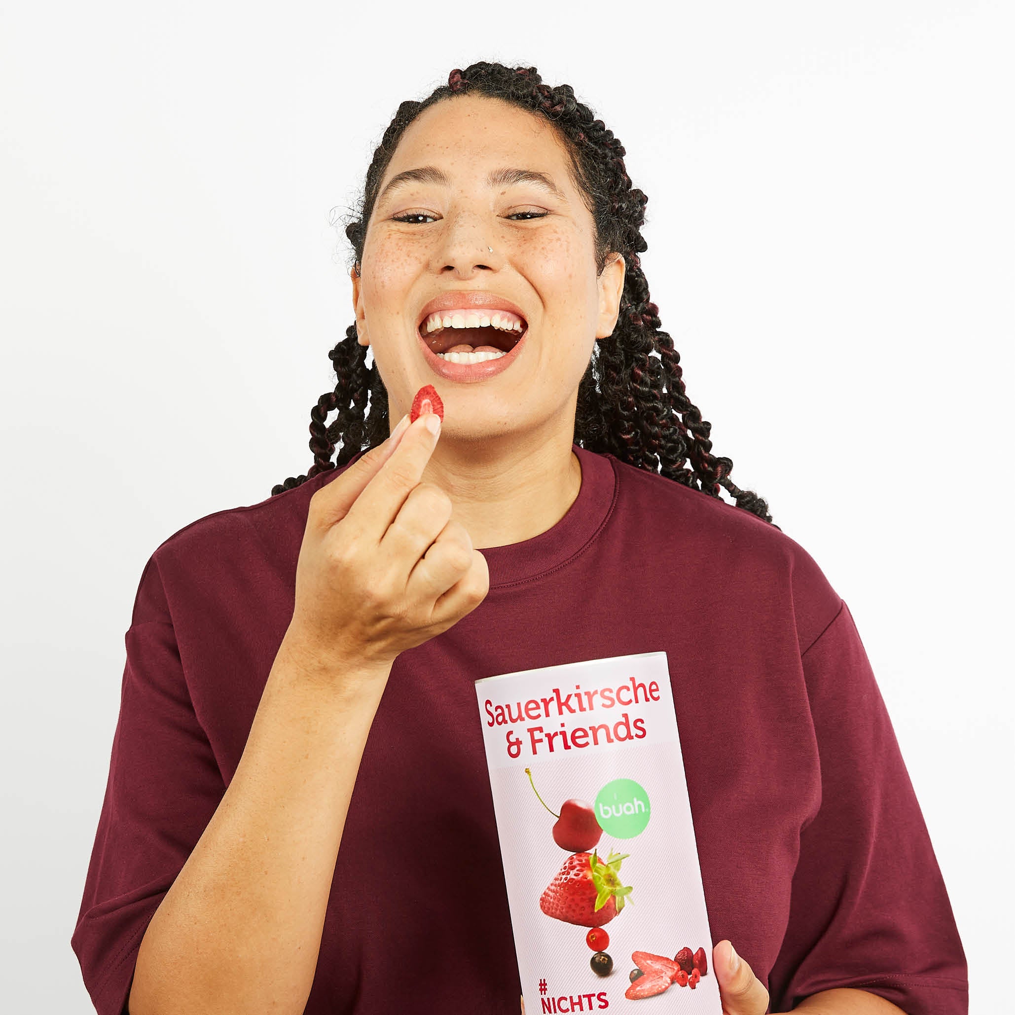 Junge Frau mit Sommersprossen und buah Sauerkirsche & Friends isst gefriergetrocknete Erdbeere