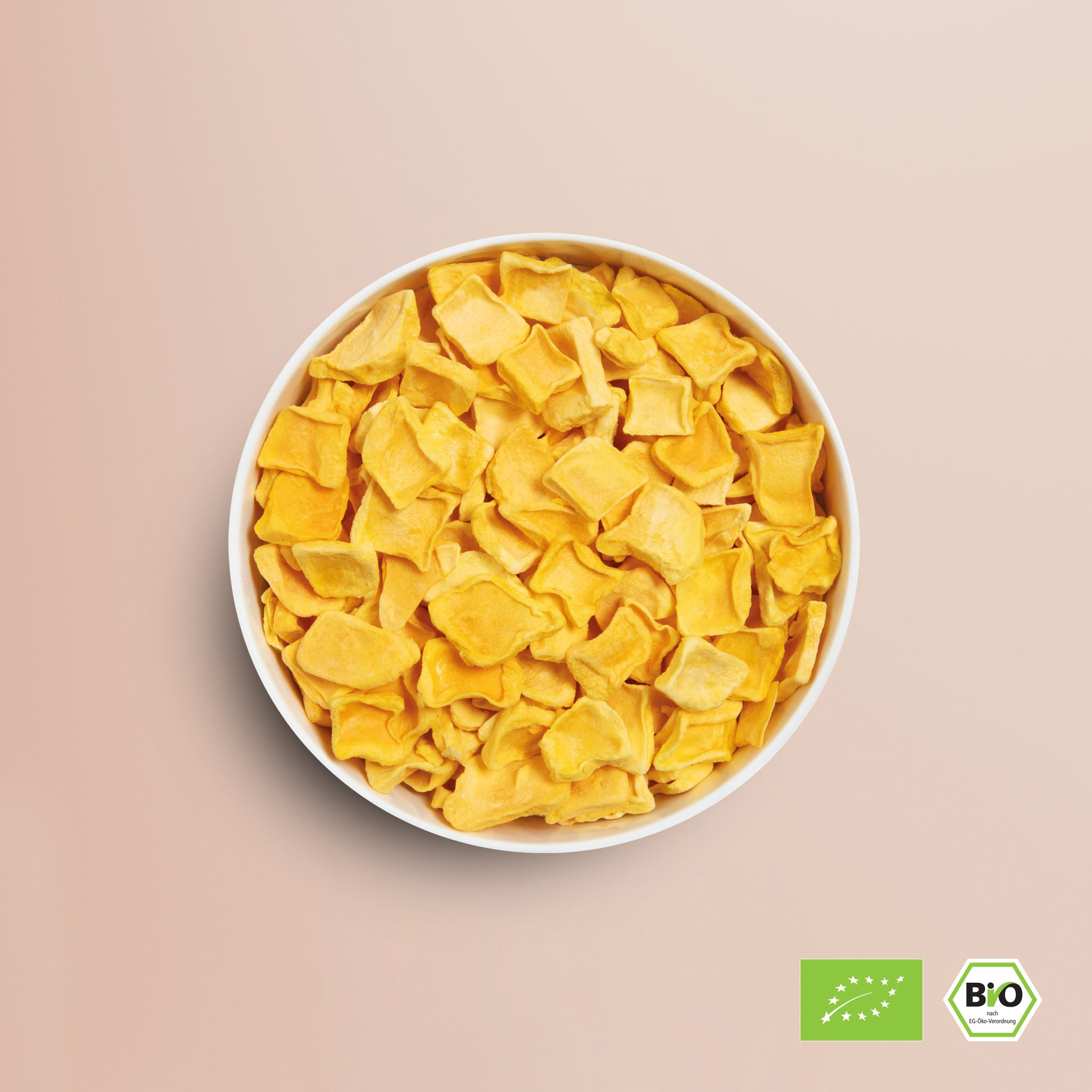 Viele buah gefriergetrocknete Mango Stuecke in einer Schale vor rosa Hintergrund