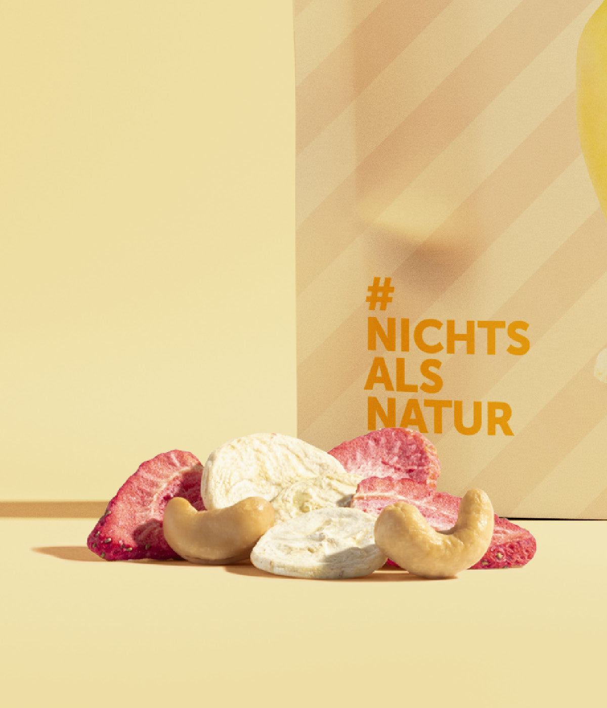 Kleiner Haufen aus gefriergetrockneten Erdbeere und Bananen gemischt mit Cashews liegt vor einer Packung buah Frucht & Nuss