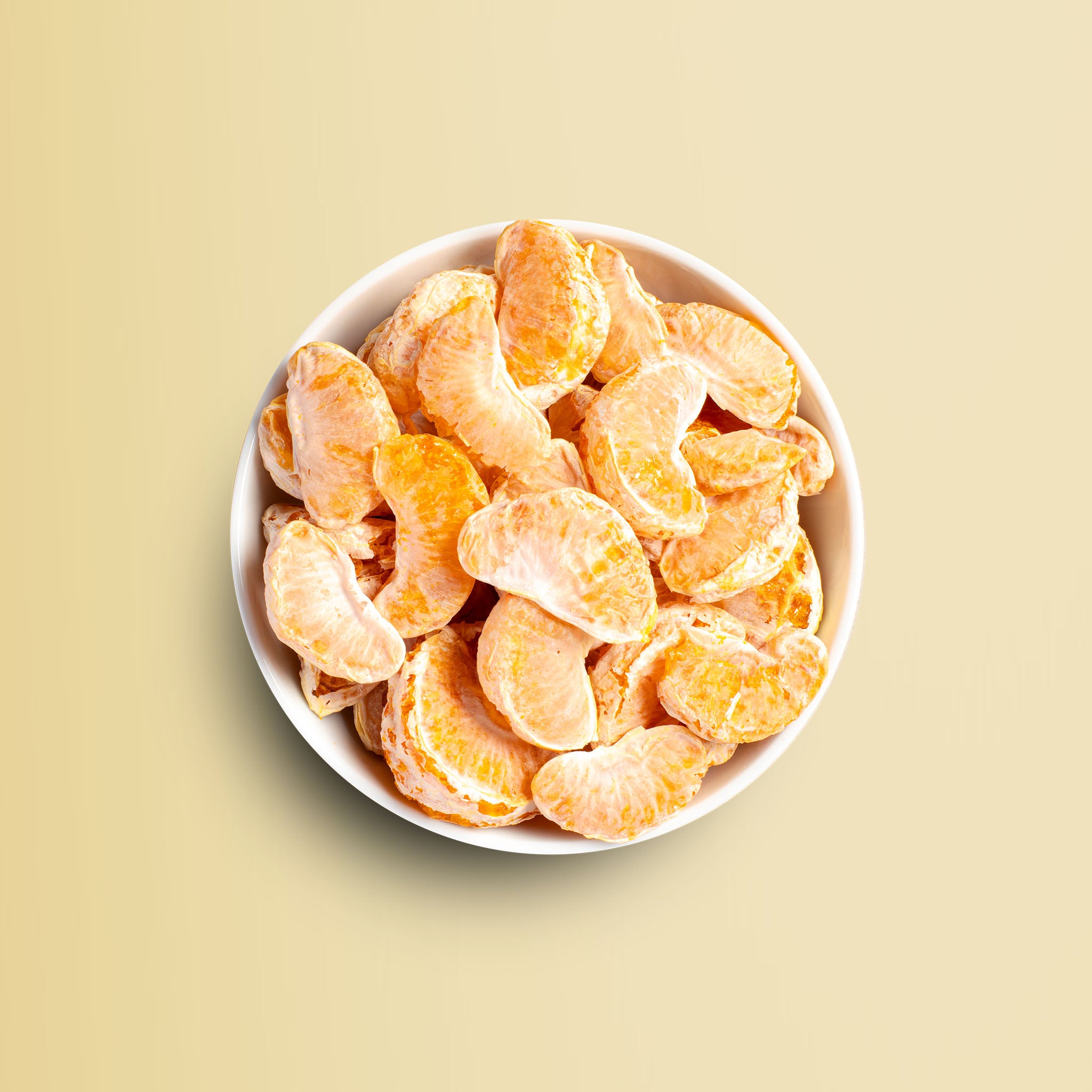 Viele buah vakuumgetrocknete Mandarinen Stücke in einer Schale vor hellgelbem Hintergrund