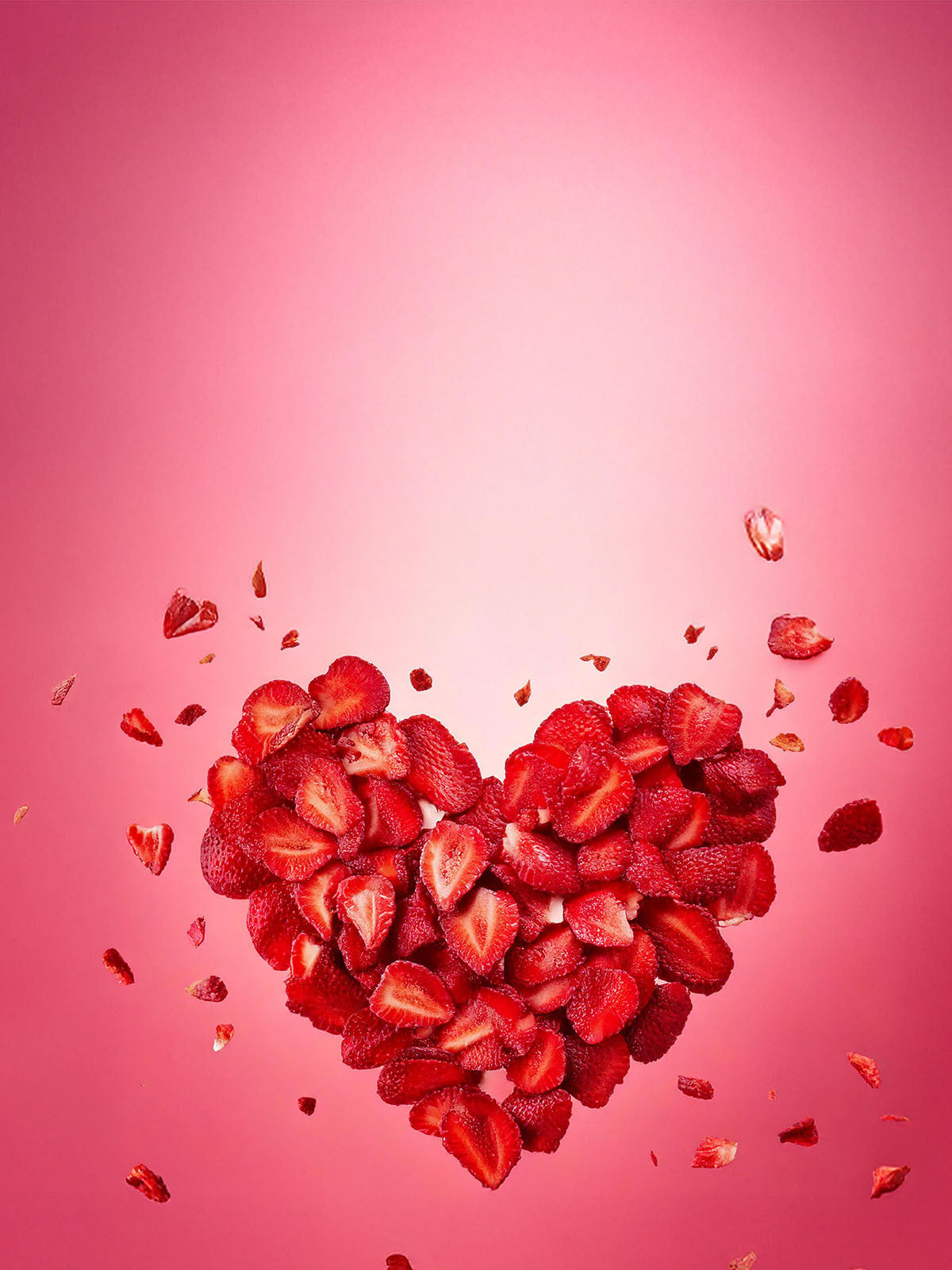 Explodierendes Valentinstag Herz aus roten buah gefriergetrockneten Erdbeeren vor rotem Hintergrund mit der Message Liebe verschenken.