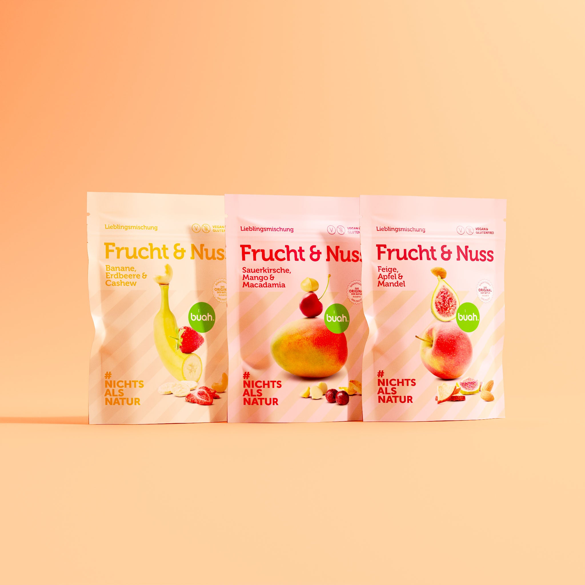 buah Frucht & Nuss Mischungen mit Banane, Erdbeere & Cashew; Sauerkirsche, Mango & Macadamia; und Feige, Apfel & Mandel stehen nebeneinander als Set vor orangenem Hintergrund. 
