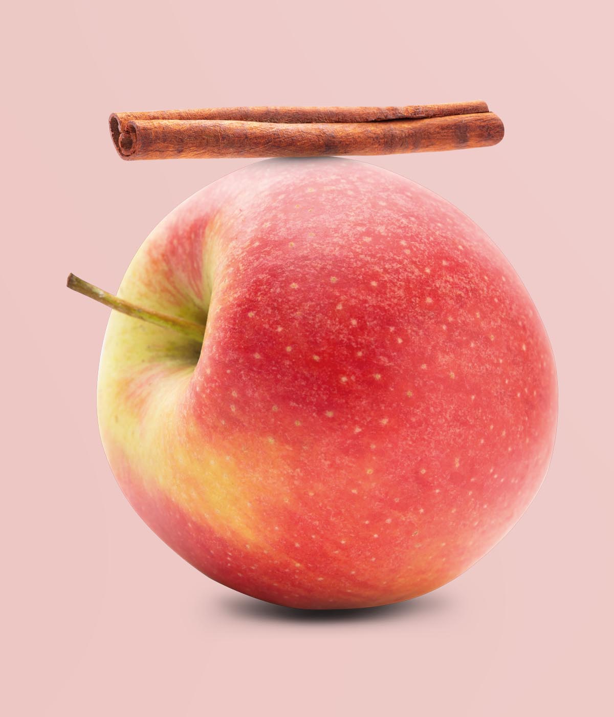 Frischer roter Apfel auf dem eine braune Zimtstange liegt vor rosa Hintergrund 