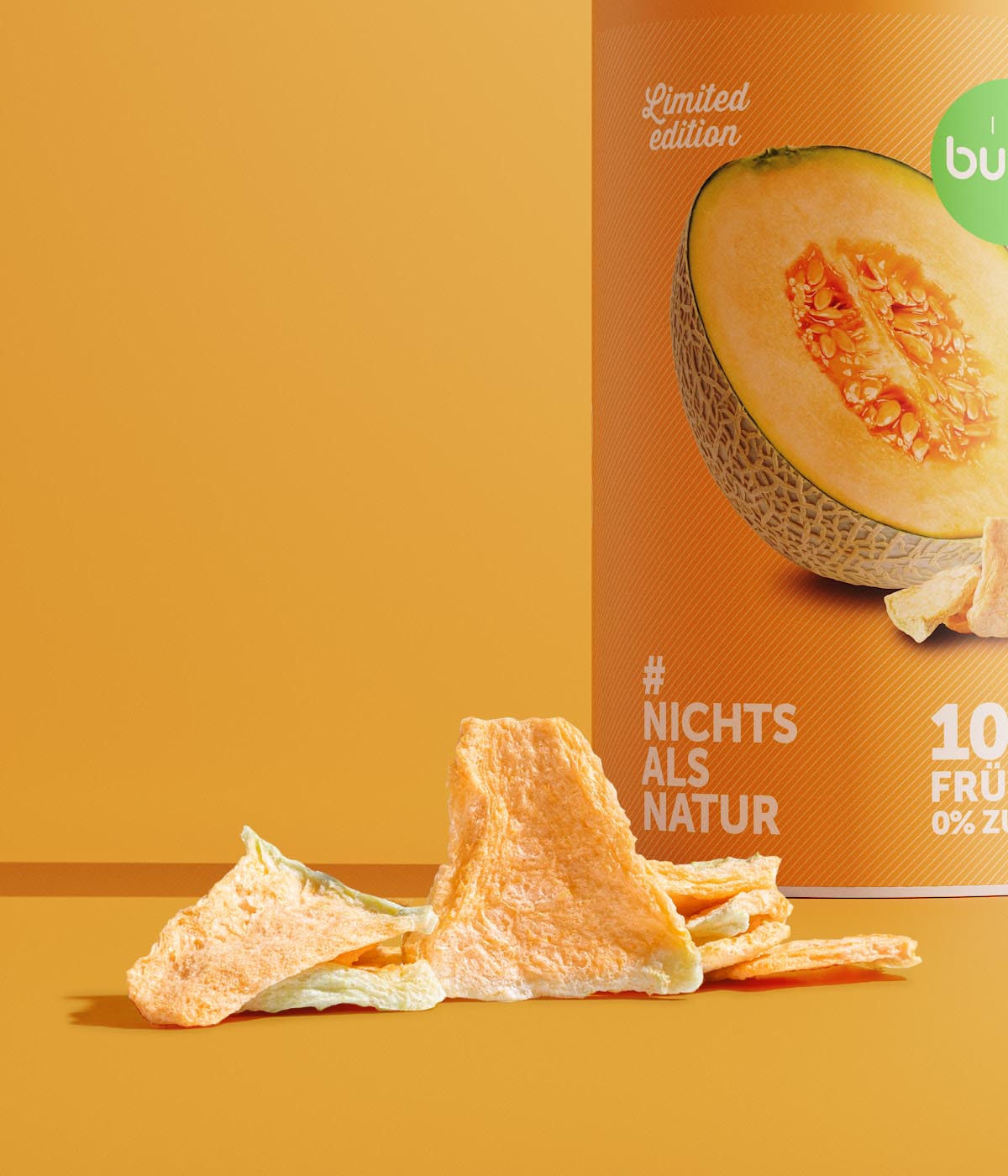 Ausschnitt der buah gefriergetrockneten Melone in der grossen Dose als limitierte Edition mit Melone Stuecken vor der Dose vor orangenem Hintergrund. 