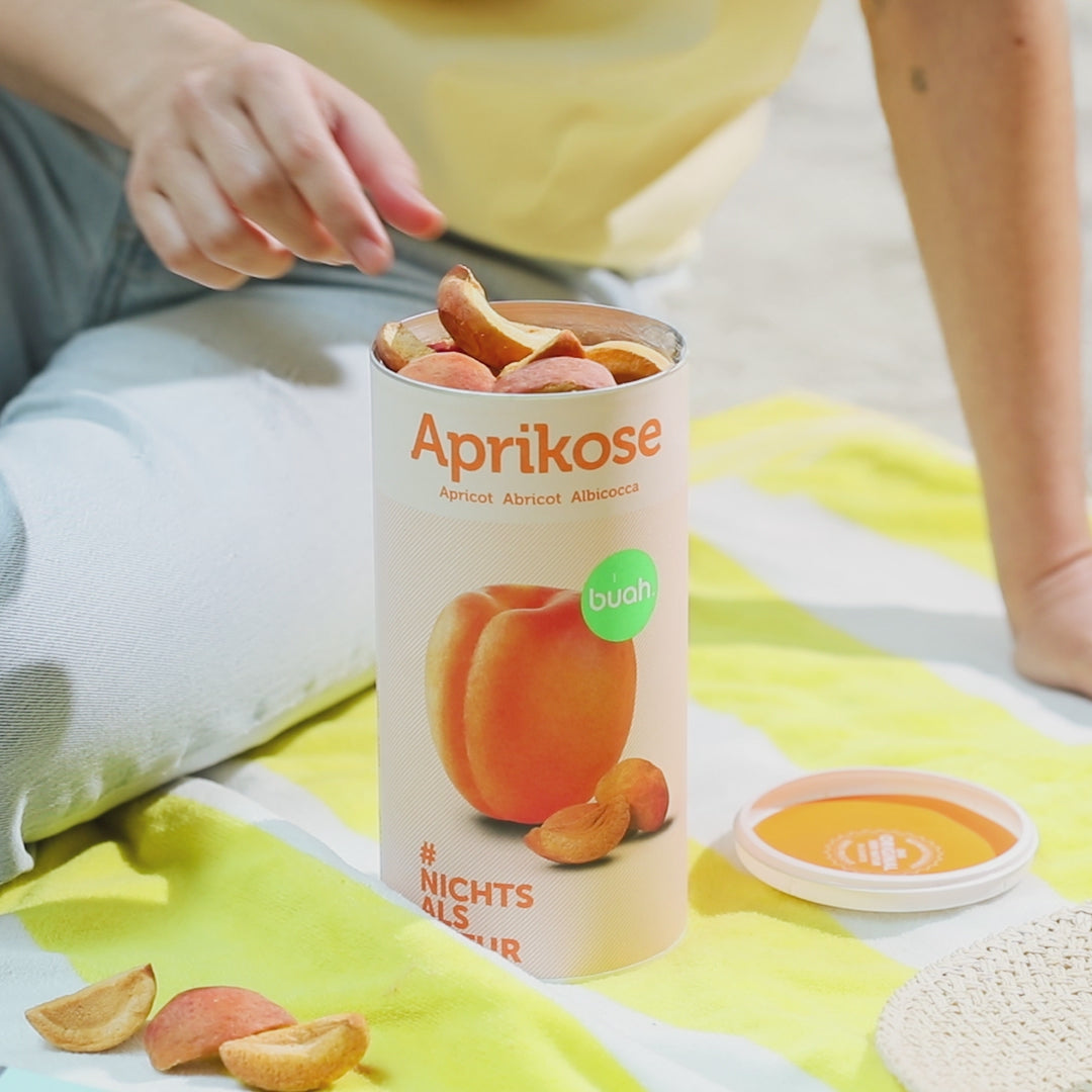 Video, wie eine Person buah Aprikose aus der Dose nimmt und auf einem gelb gestreiftem Handtuch sitzt 